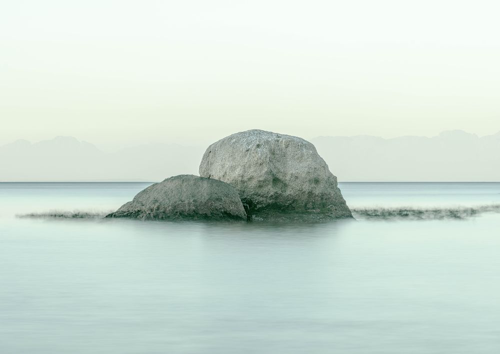 Two boulders in still water, mountains beyond
