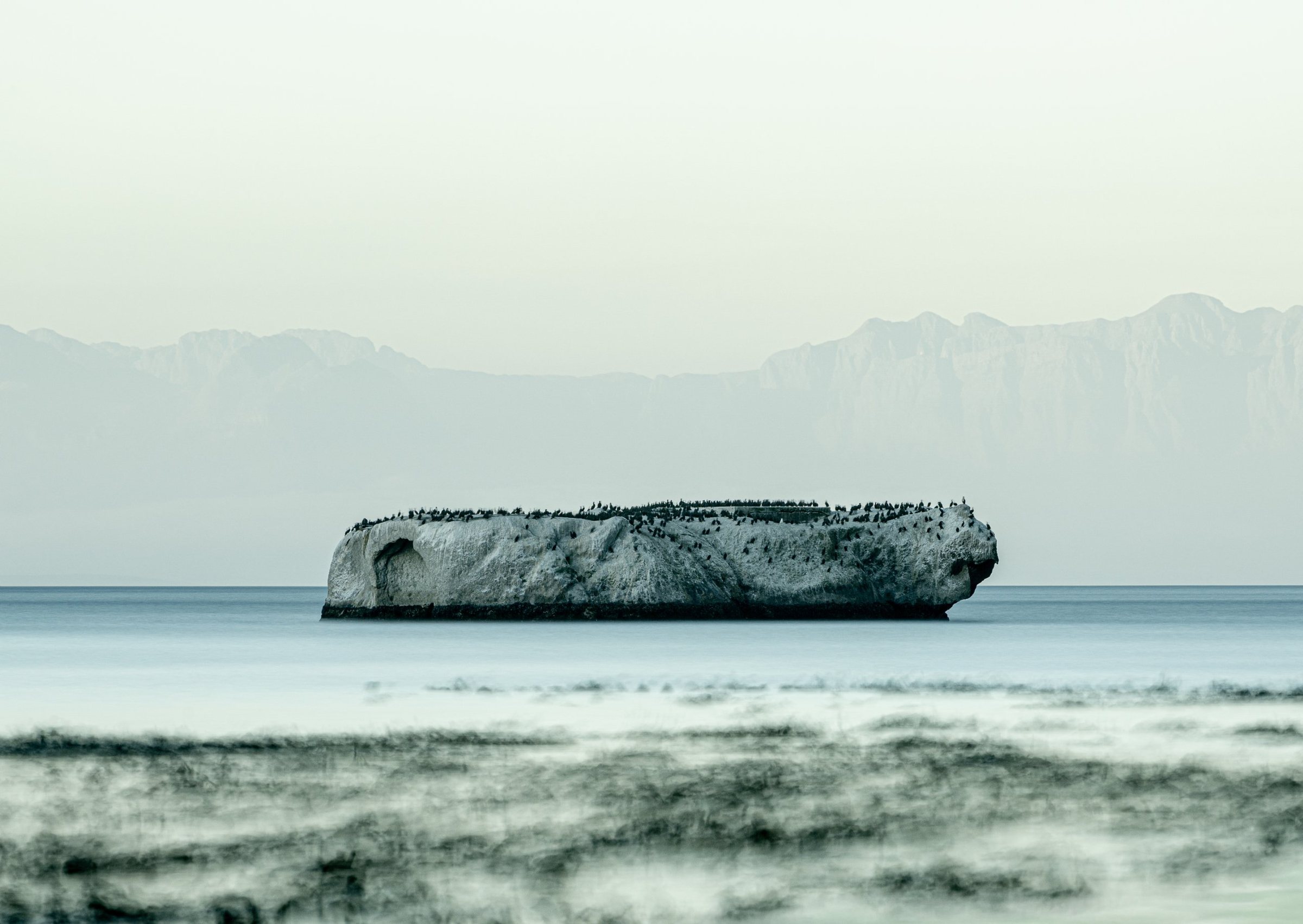 The Arc — a pale rock island under a haze of mountains, Before Time